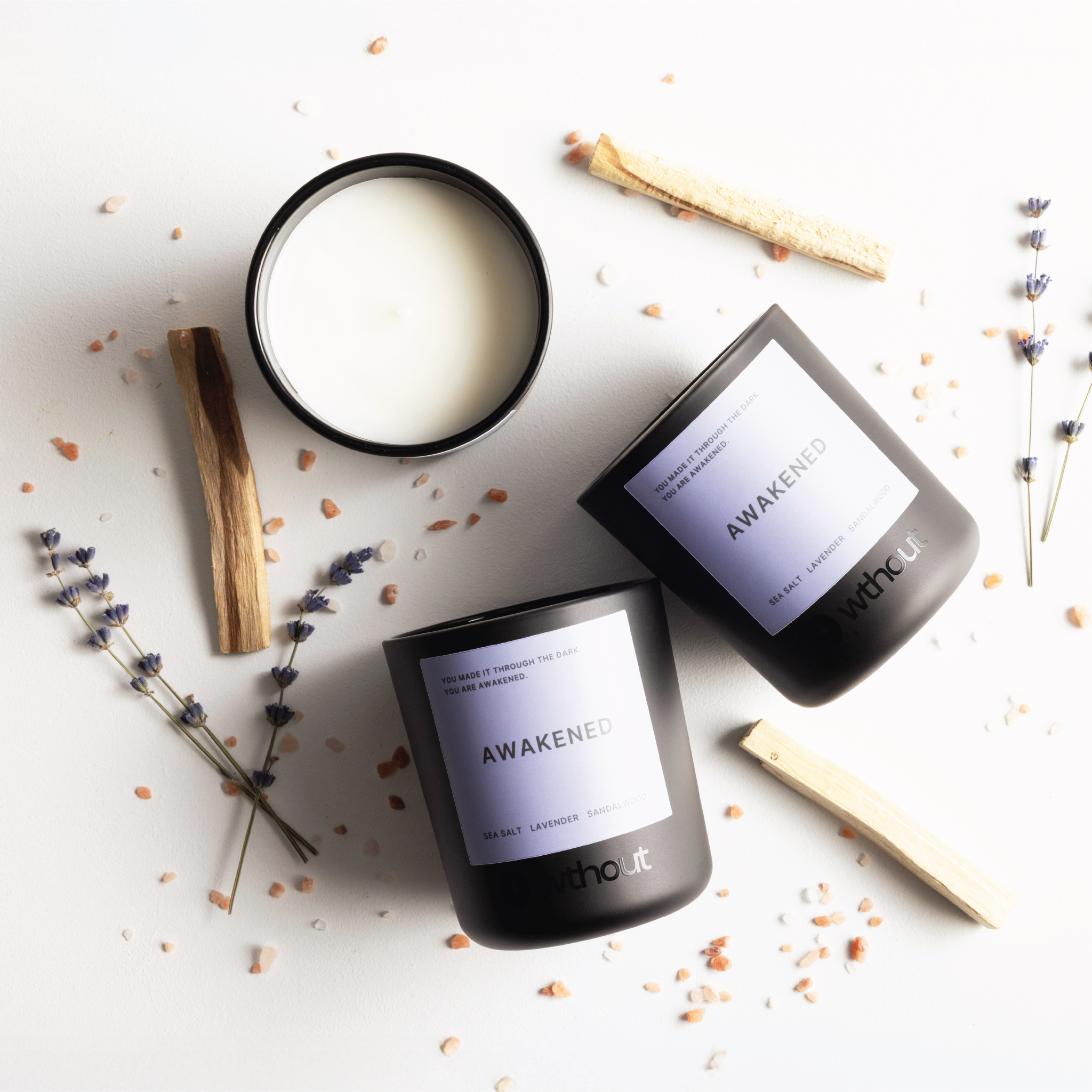 Three 'Awaken' candles on a light surface with lavender and wooden sticks.