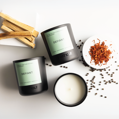 Candle with 'Defiant' label and wooden sticks on a white background