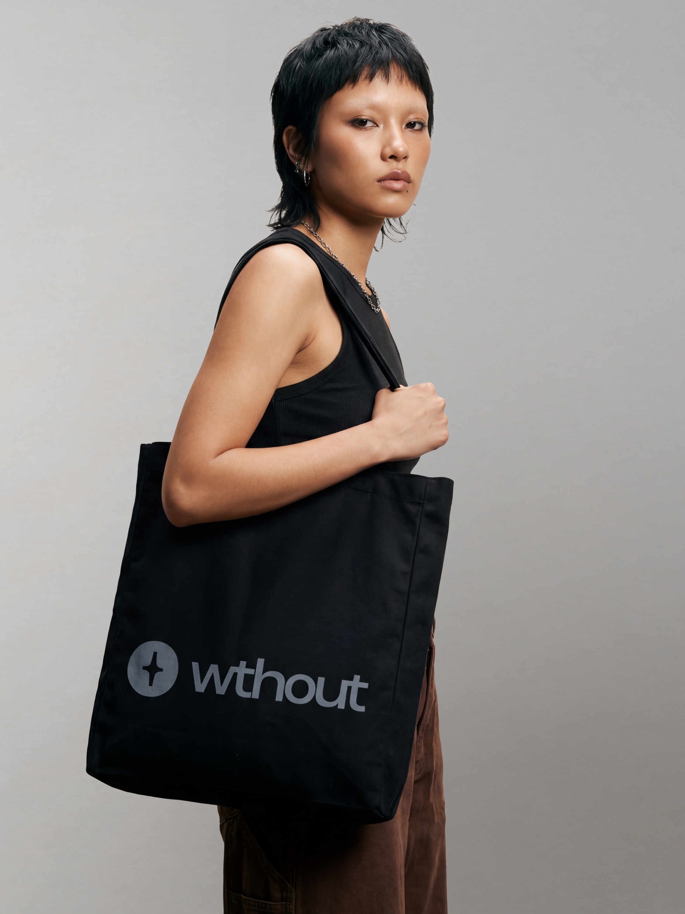 Person holding a black tote bag with 'without' branding against a gray background