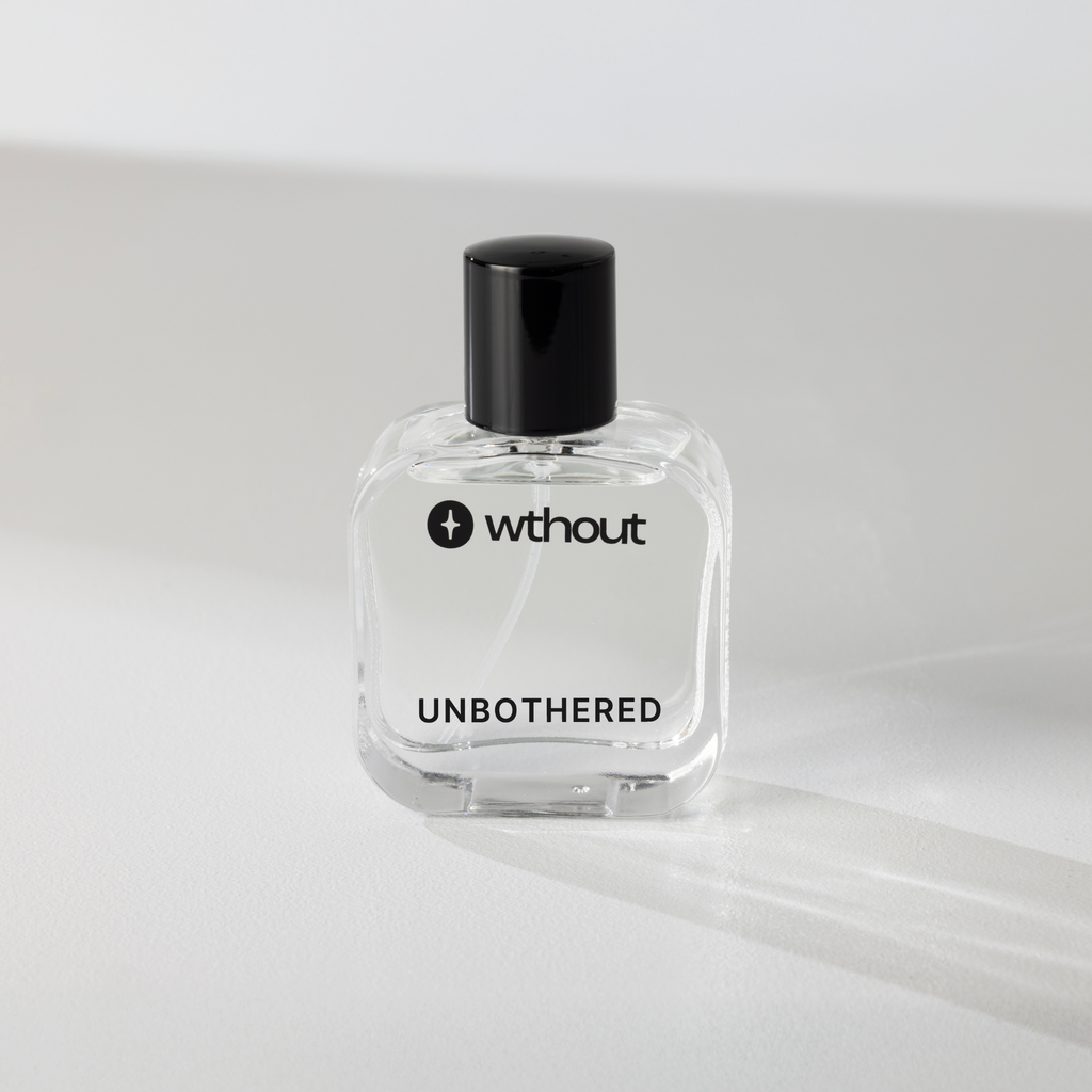 Clear perfume bottle with black cap labeled 'without unbothered' on a light gray background